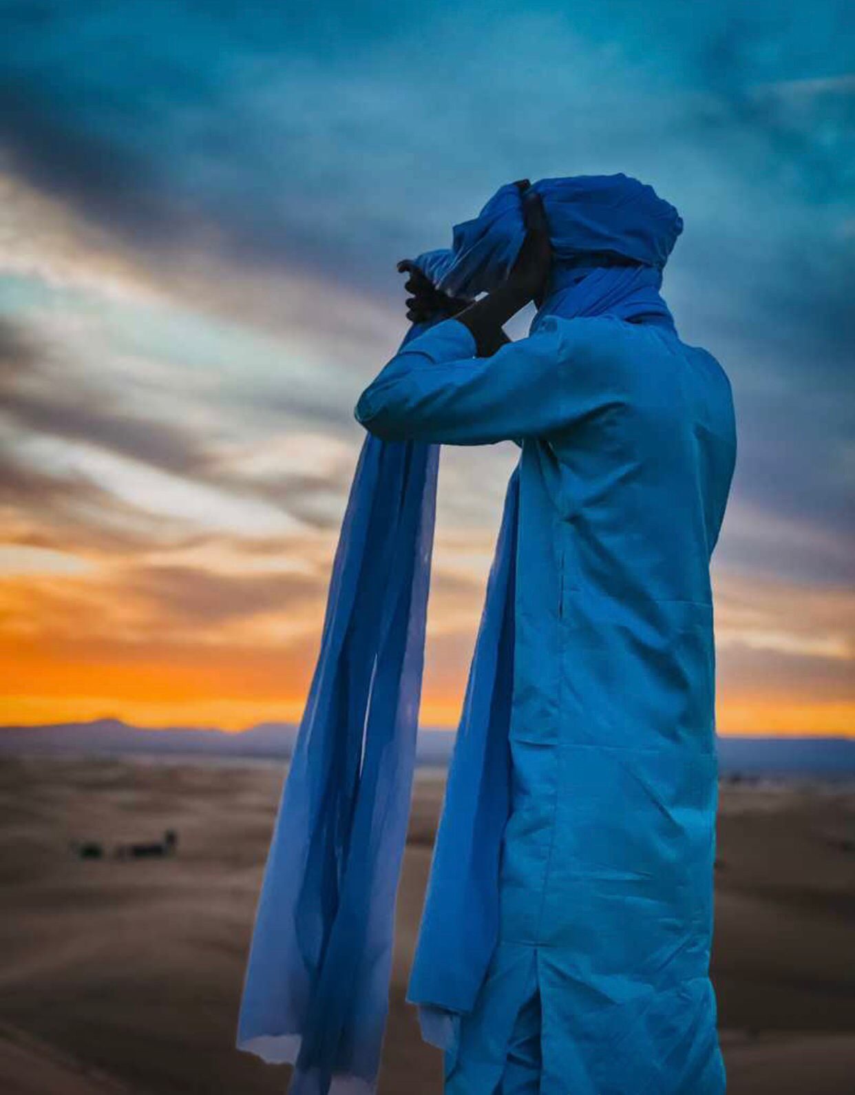 Guía con túnica azul atándose el turbante al atardecer en el desierto